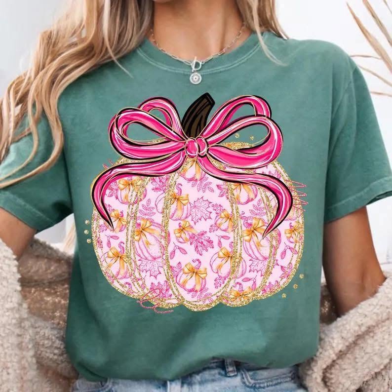 Pink and gold patterned pumpkin with pink bow on green shirt